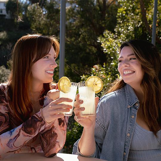 Two young caucasian women are sitting on a patio drinking lemonade.