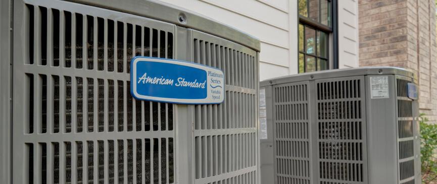 Two outdoor American Standard heating and cooling systems are pictured with a close up of the brand label