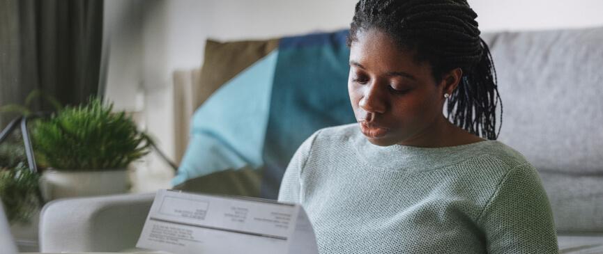 A woman sits inn her living room while looking at her latest energy bill.