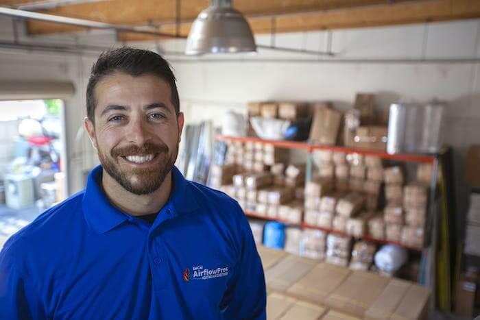 Cody Novini, of SoCal Airflow Pros, stands in a garage space amid brown boxes.